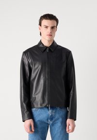 Black leather jacket with a collared neckline and front zipper, featuring a smooth texture and long sleeves, paired with blue denim jeans.