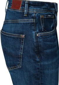 Tumši zili džinsa džinsi ar redzamām šuvēm, priekšējām un aizmugurējām kabatām, metāla kniedēm un brūnu Pepe Jeans ādas zīmola uzlīmi.