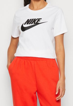 Osoba nosząca białą koszulkę Nike z czarnym logo i jaskrawo pomarańczowe spodnie, ręce swobodnie opuszczone wzdłuż boków.
