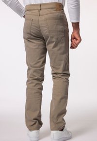 Pantaloni in cotone beige con taglio dritto, due tasche posteriori, cuciture in vista e un'etichetta in pelle marrone in vita. Sneakers bianche.