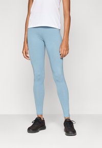 Lys blå leggings laget av et elastisk materiale, tettsittende design og en glatt tekstur. Brukt med en hvit t-skjorte og svarte treningssko.