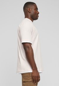 Lyserød t-shirt med korte ærmer og hvid kant ved manchetterne, afslappet pasform, lavet af blødt bomuldsstof. Set fra siden.