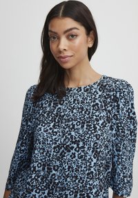 Blusa floreale blu con motivi floreali neri, scollo rotondo e maniche a puff a tre quarti. Tessuto liscio con una vestibilità rilassata.