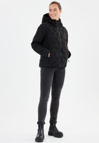Svart vadderad pufferjacka med huva, framdragkedja och sidofickor, kombinerad med mörkgrå skinnyjeans och svarta klumpiga ankelstövlar.