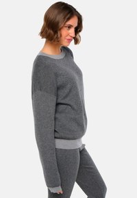 Pull en maille gris avec un col rond et des manches longues, présentant un motif texturé et un ourlet côtelé et des poignets contrastants.