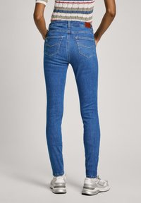 Jeans ajustados de mezclilla azul con una textura suave, cintura alta y dos bolsillos traseros. Llevados con zapatillas grises y una camiseta a rayas.