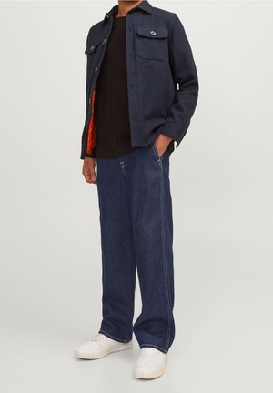 Marineblauwe wollen blendjas met knopen, twee borstzakken en een oranje voering, gecombineerd met lichtblauwe wijde denim broeken en witte sneakers.