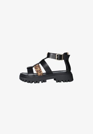 Sandalo nero con suola chunky, cinturino con stampa leopardata e fibbia dorata sulla cinghia alla caviglia, vista laterale su sfondo bianco.