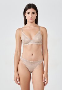 Spitzen-BH und passendes Tanga-Set in hellem Beige. Mit zarten gewellten Kanten, schmalen Trägern und einem kleinen Schleifendetail am Tanga.
