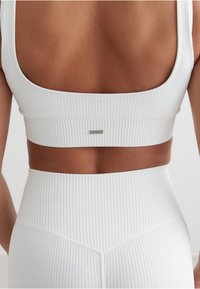 Hvit stripete sports-bh med bred halsringning og en sølv logo-lapp på baksiden, sammen med matchende høyt belte stripete leggings.