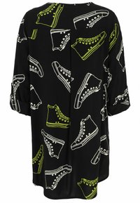 Schwarze Tunika mit weißen und neon-grünen grafischen Designs verschiedener Sneakers. Sie hat eine lockere Passform und Dreiviertelärmel.