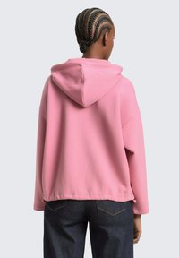 Roze sweatshirt met capuchon en lange mouwen, een comfortabele pasvorm, geribbelde zoom en een gestructureerde stof, gecombineerd met een donkere spijkerbroek.