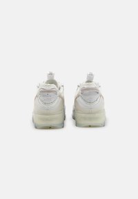 Ett par vita Nike-sneakers med Crater Foam-sulor sedda från baksidan, med detaljer i mesh och läder samt dragflikar.