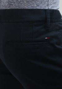 Svarta byxor i vävt tyg med en slät yta, med en bakficka med en liten röd, vit och blå logodetalj.