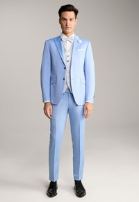 Helles blaues Anzugensemble mit einem einreihigen Sakko, passenden Hosen und einem weißen Hemd mit strukturiertem Muster. Schwarze Dressschuhe runden den Look ab.