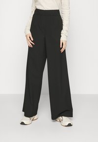 Black wide-leg trousers with an elastic waistband, made from a smooth fabric. Paired with a light long-sleeve top and sporty shoes.