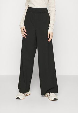 Pantalons larges noirs avec une taille élastique, fabriqués dans un tissu lisse. Assortis à un haut léger à manches longues et des chaussures de sport.