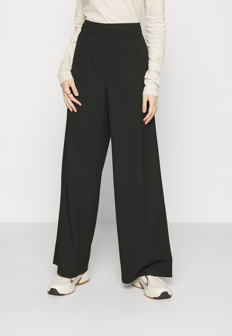 Black wide-leg trousers with an elastic waistband, made from a smooth fabric. Paired with a light long-sleeve top and sporty shoes.