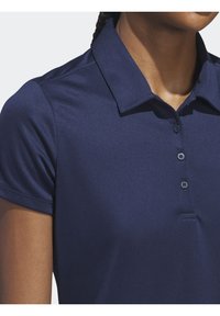 Námořnická modrá polokošile s límečkem, krátkými rukávy a knoflíky. Vyrobena z hladké tkaniny s jemným leskem a přiléhavým střihem.