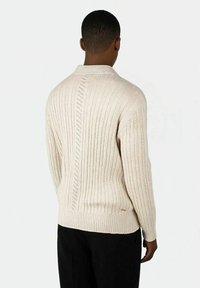 Beige ribbestrikket genser med krage, som har et vertikalt mønster og subtil detaljering. Fitted form med strukturert finish.