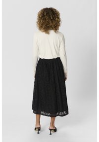 Zwarte maxi-spitzenrok met een gestructureerd patroon en elastische tailleband, gecombineerd met een witte top met lange mouwen met kantafwerking op de mouwen.