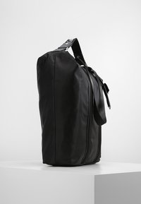 Zwarte nylon schoudertas met een ritssluiting, rechthoekige vorm, verstelbare schouderriem en een gestructureerd oppervlak. Kenmerkt een slank ontwerpaccent.