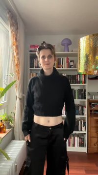Black ribbed cropped sweater with a high, folded collar, paired with high-waisted black satin pants featuring side pockets.