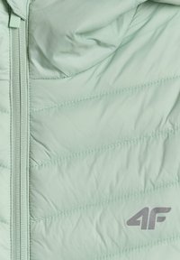 Partie de veste matelassée vert clair avec fermeture éclair verticale à gauche et logo gris « 4F » en bas à droite.
