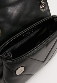 Svart läderhandväska med quiltat mönster, silverfärgad metallbeslag och magnetlås på framfickan. Insidan har ett slätt foder.