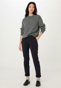 Šedý pletený svetr s uvolněným střihem, kombinovaný s tmavě modrými kalhotami s ohrnutými manžetami. Černé loafery zvýrazňují celý outfit.