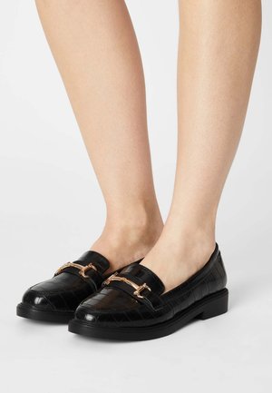 Sorte læder loafers med en blank krokodille-tekstur, der har en guldfarvet hardware accent og en lav, robust sort hæl.