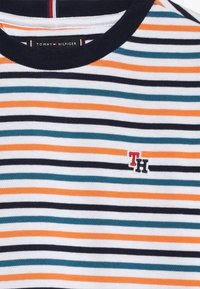 Raidallinen lyhythihainen paita, jossa on tummansinisiä, oransseja, teal-värisiä ja valkoisia raitoja. Pyöreä pääntie, jossa on Tommy Hilfiger -logo brodeerattuna rintaan.