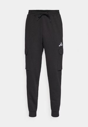 Un pantalon de survêtement noir avec une taille à cordon de serrage, des jambes fuselées et deux poches cargo sur les côtés. Il est orné d'un petit logo Adidas gris sur la cuisse gauche.
