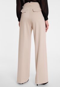 Wijde broeken van een zachte beige stof. Heeft een hoge taille met accent rugzakken en een gladde textuur.