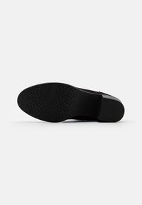 Suola di scarpa nera con un motivo di grip testurizzato, design angolare e un leggero tacco. Realizzata in materiale sintetico, presenta una finitura liscia.