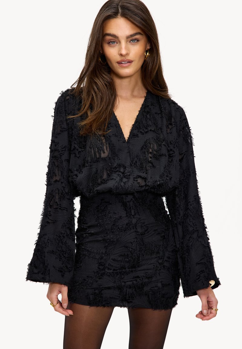 Zwarte jurk met lange mouwen, textuurstof met verheven patronen, diepe V-hals, aansluitende taille en uitlopende mouwhems.
