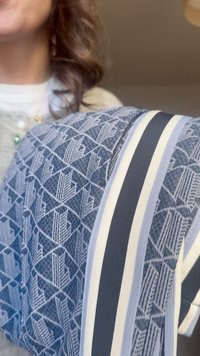 Frau hält einen blauen Stoff mit geometrischen Mustern und vertikalen weißen, grauen und schwarzen Streifen, dabei sind teilweise ihr Hals und lockiges Haar zu sehen.