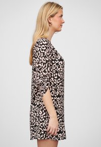 Leopardin kuosi mekko mustalla pohjalla, jossa on vaaleanpunaisia täpliä. Pitkät hihat käännetyillä'ihi'kenillä, pyöreä pääntie ja rento malli.