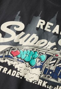 Czarny bawełniany t-shirt z grafiką pociągu ozdobionego niebieską i czerwoną graffiti. Na tle miasta znajduje się biały napis "REAL Super".