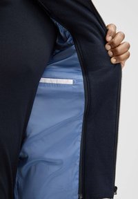 Granatowa kurtka z gładką, niebieską podszewką i zapinaną na zamek kieszenią wewnątrz. Zewnętrzny materiał jest teksturowany, zapewniając ciepło i komfort.