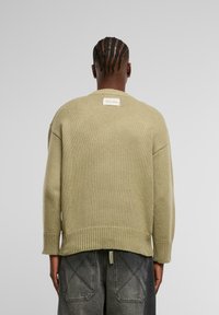 Olivgrüner Strickpullover mit geripptem Saum und Bündchen, ausgestattet mit einem Markenlabel im Nackenbereich und einem lockeren, entspannten Schnitt.