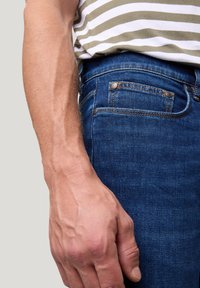 Donkerblauwe denim jeans met een gladde textuur. Beschikt over een vijf-vakken ontwerp en koperen hardware accenten. Hand ligt casual aan de zijkant.