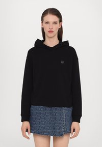 Svart hettegenser laget av bomull, med en tettsittende design. Kombinert med et denim skjørt som viser et geometrisk mønster.
