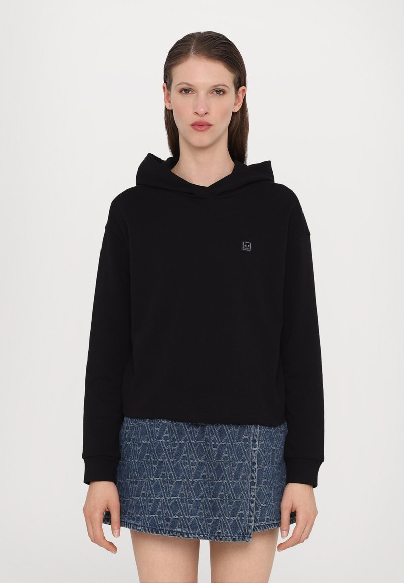 Svart hettegenser laget av bomull, med en tettsittende design. Kombinert med et denim skjørt som viser et geometrisk mønster.