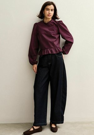 Maroon peplum top with puffed sleeves, paired with loose dark denim pants and brown flats. Smooth fabric with a textured sleeve design.