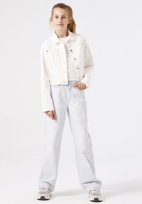 Chaqueta de mezclilla blanca recortada con cierre de botón, dos bolsillos frontales, combinada con jeans rectos de color azul claro y zapatillas neutras.