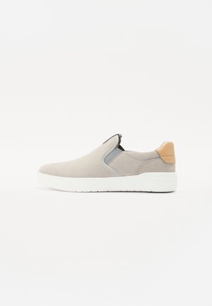 Baskets slip-on gris clair en suède, avec des panneaux latéraux élastiques et un accent en cuir tan au niveau du talon. Semelle extérieure blanche en caoutchouc.