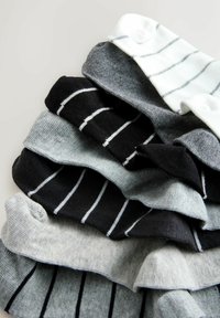 Pile de chaussettes pliées en noir, blanc et différentes nuances de gris avec des motifs à rayures horizontales et verticales sur un fond clair.