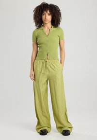 Light green ribbed short-sleeve button-up top paired with loose, flowing light green pants and chunky black footwear.