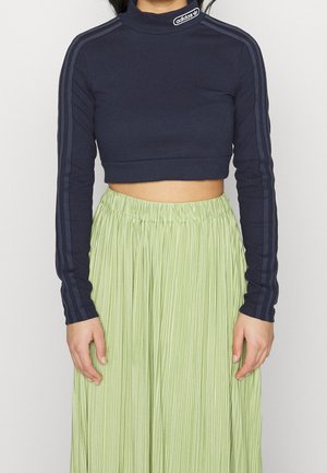 Topp long-sleeve av navy blue Adidas med cropped design, logo på kragen og striper på ermene, kombinert med et lyst grønt plissert skjørt.